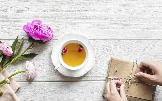 Žena zväzuje hnedé obálky na bielom stole, na ktorom je šálka s čajom a ruže.jpg